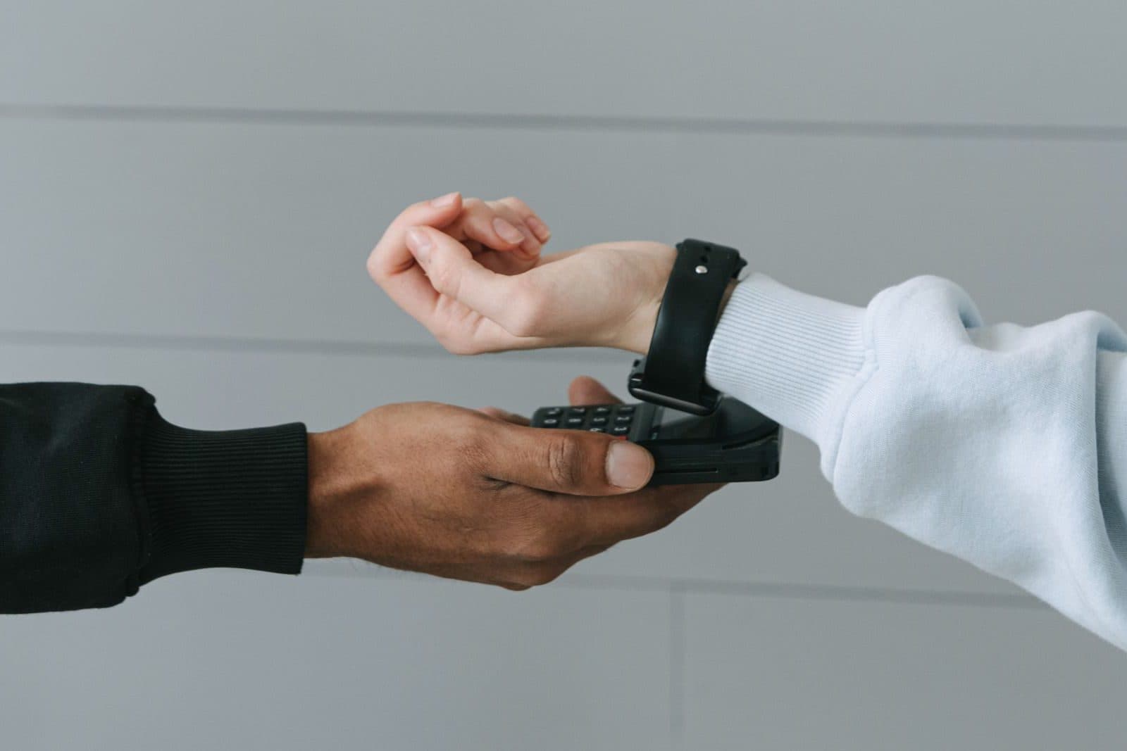 Eine Kundin tippt mit ihrer Smartwatch auf das Kartenterminal in der Hand der Kassiererin